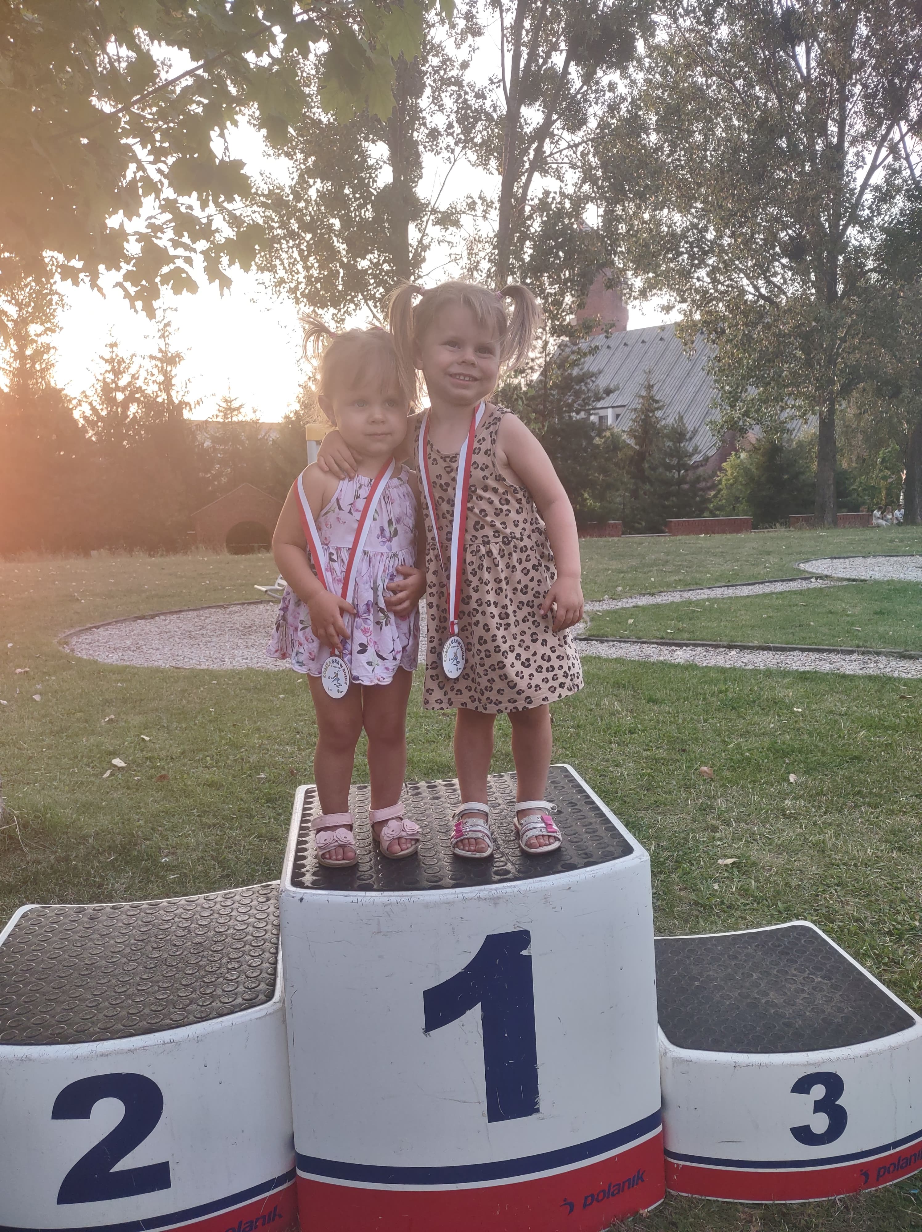 Dwie dziewczynki z medalami stoją na 1 miejscu podium.