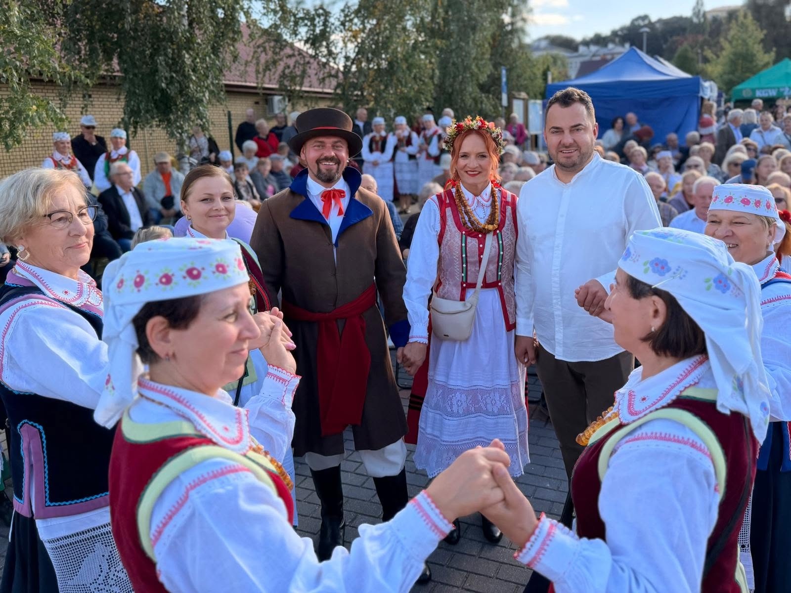 Zdjęcie przedstawia Prezydenta Miasta Łomży, panią Dyrektor MOSiR Łomża oraz inne osoby, które trzymają się za ręce podczas tańca na łomżyńskich bulwarach.